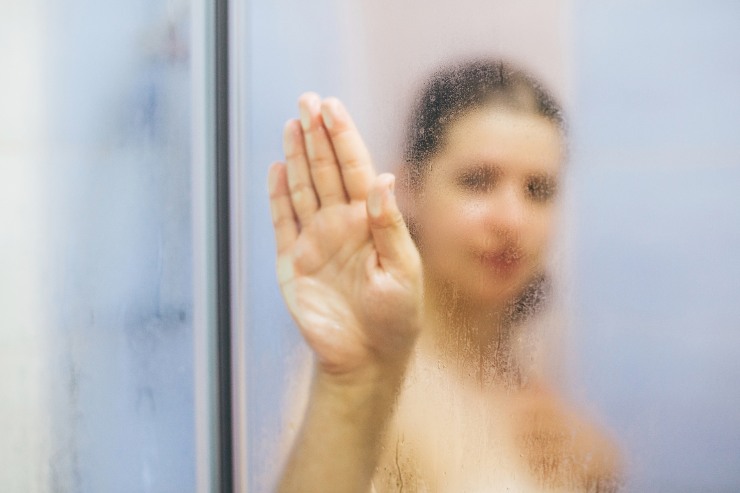 Donna sotto la doccia che mette la mano sul vetro appannato dall'acqua calda