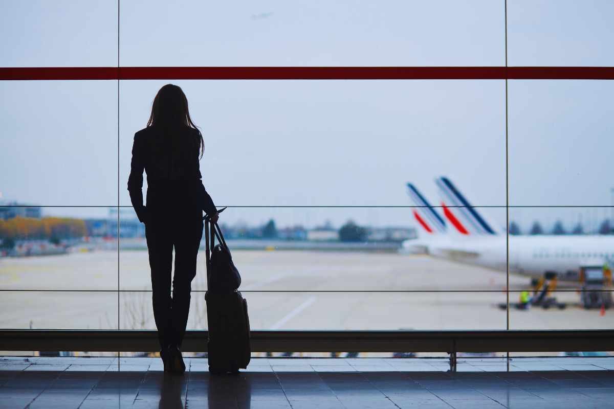 Donna in aeroporto che osserva un aereo dal vetro del Gate